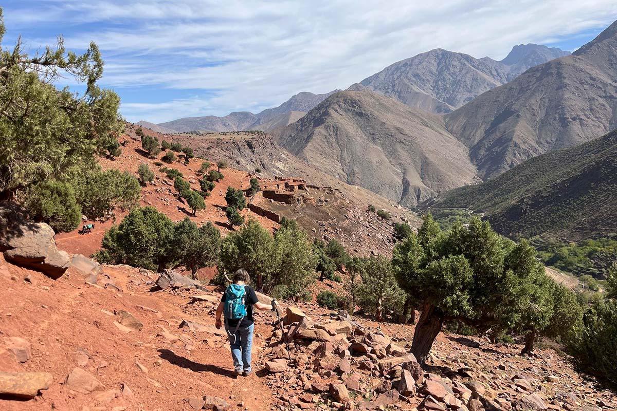 Hiker descending a red earth trail in Azzaden Valley with mountain views