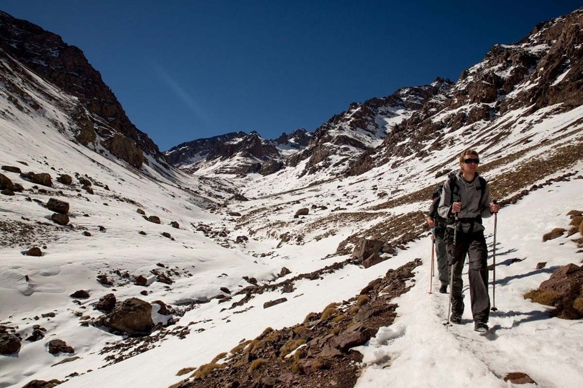 Hiker trekking with poles on a snowy mountain trail in the High Atlas Mountains