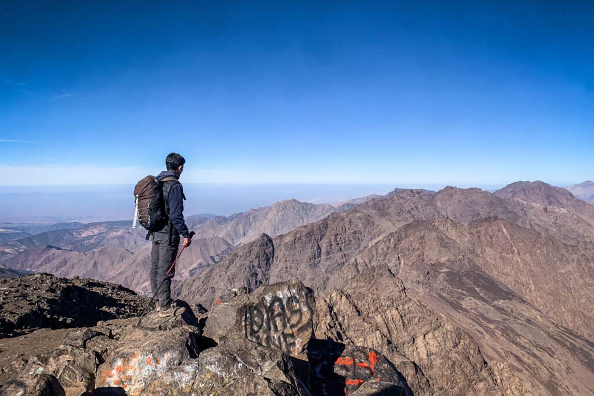 Hiker standing on Mount Toubkal summit with panoramic views of the High Atlas Mountains