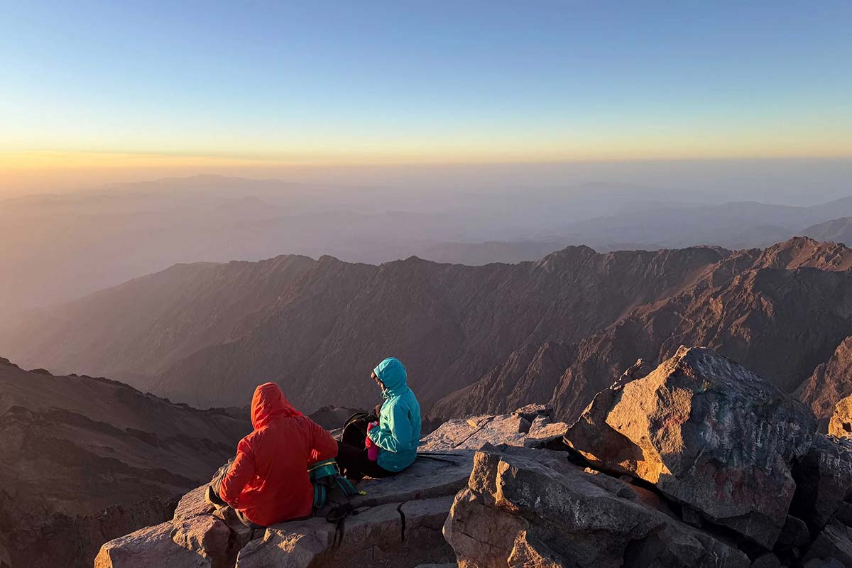 Trekkers resting on Mount Toubkal summit at sunrise with panoramic High Atlas views