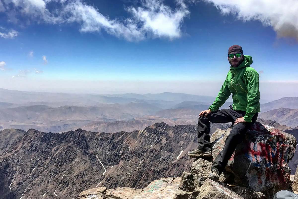 Hiker sitting on Mount Toubkal summit with panoramic views of the High Atlas Mountains in Morocco